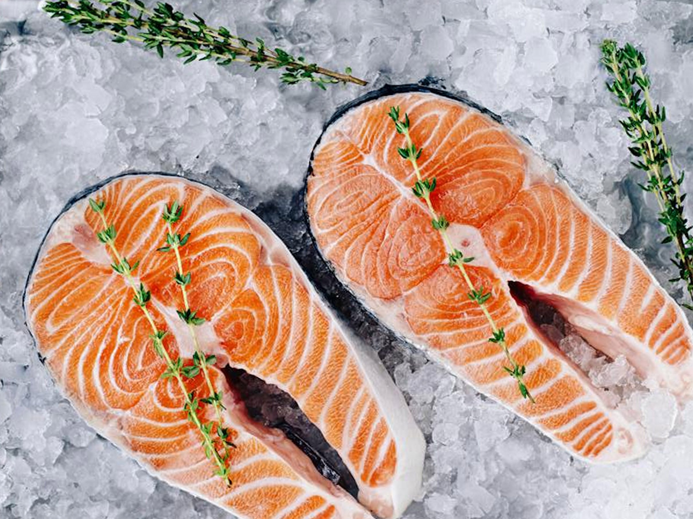 Two fillets of raw salmon with sprigs of fresh thyme on a bed of crushed ice.