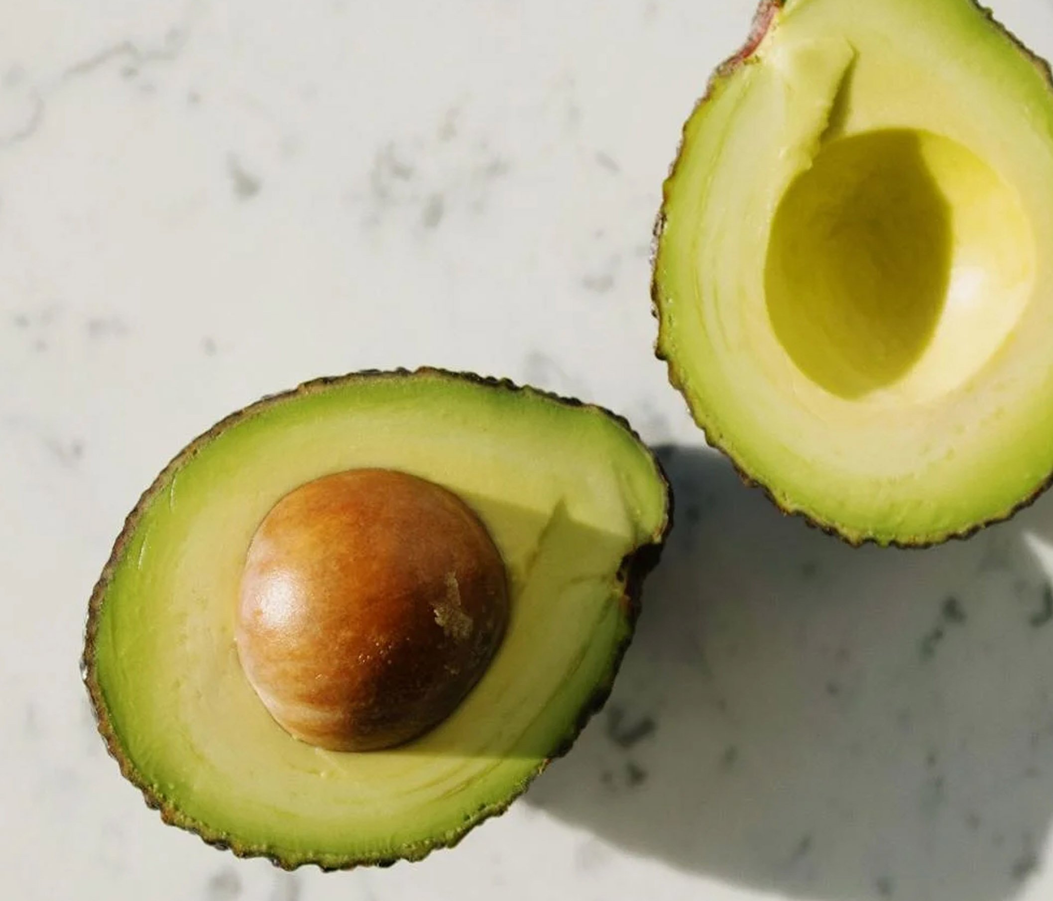 Half of an avocado with the seed still inside, placed on a white surface.