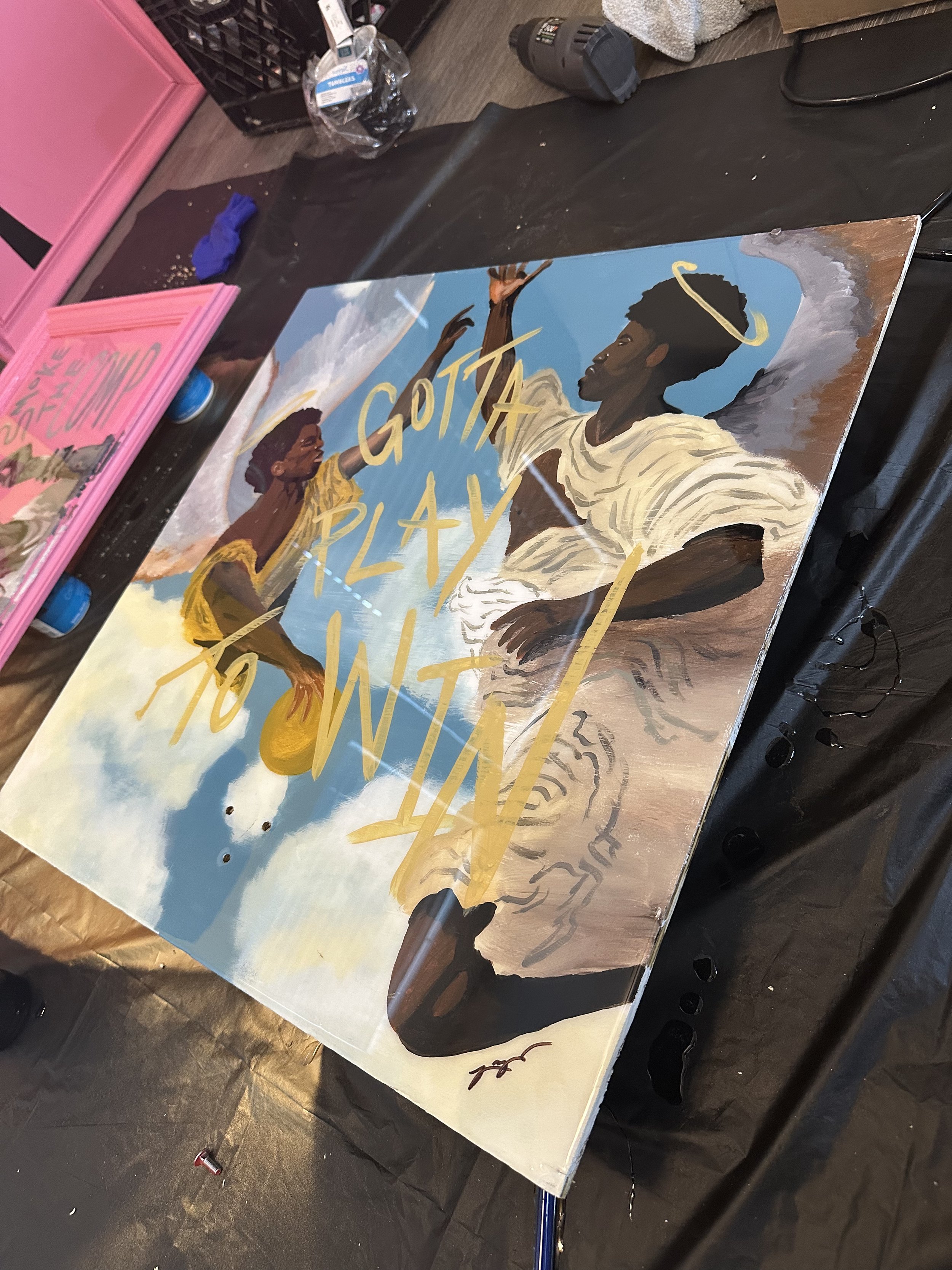 A painting featuring a dark-skinned man with an afro hairstyle, wearing a cream-colored shirt with rolled-up sleeves, and a halo above his head. A smaller figure to the left, also dark-skinned with short hair and a yellow outfit, appears to be reaching towards the larger figure in the sky. The background includes a sky with clouds and golden cursive text that reads 'GOTTA PLAY'.