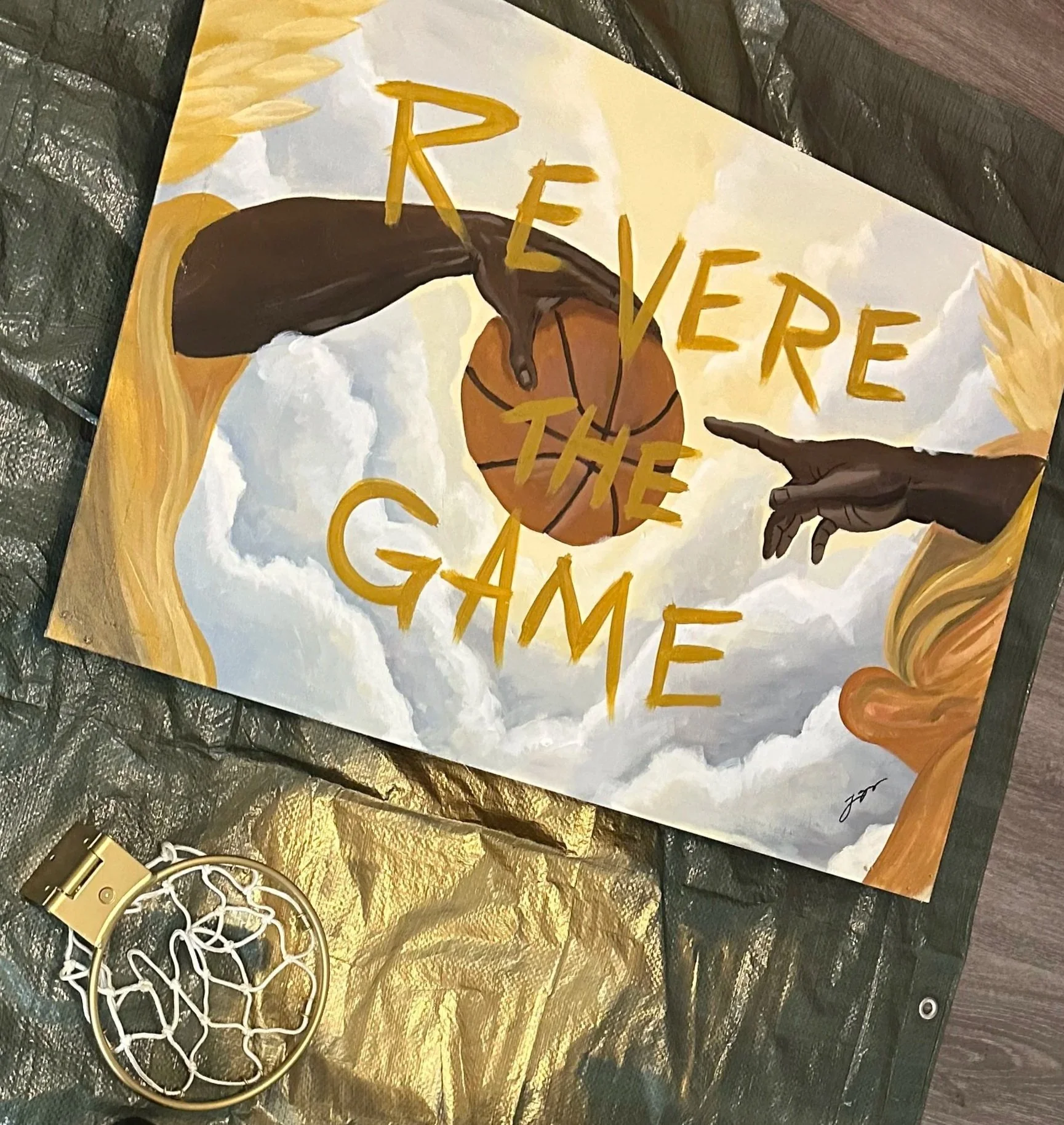 A painted sign with the words 'RELEASE THE GAM' in yellow letters, a basketball illustration, and hands painted next to the lettering, with a gold and black background.