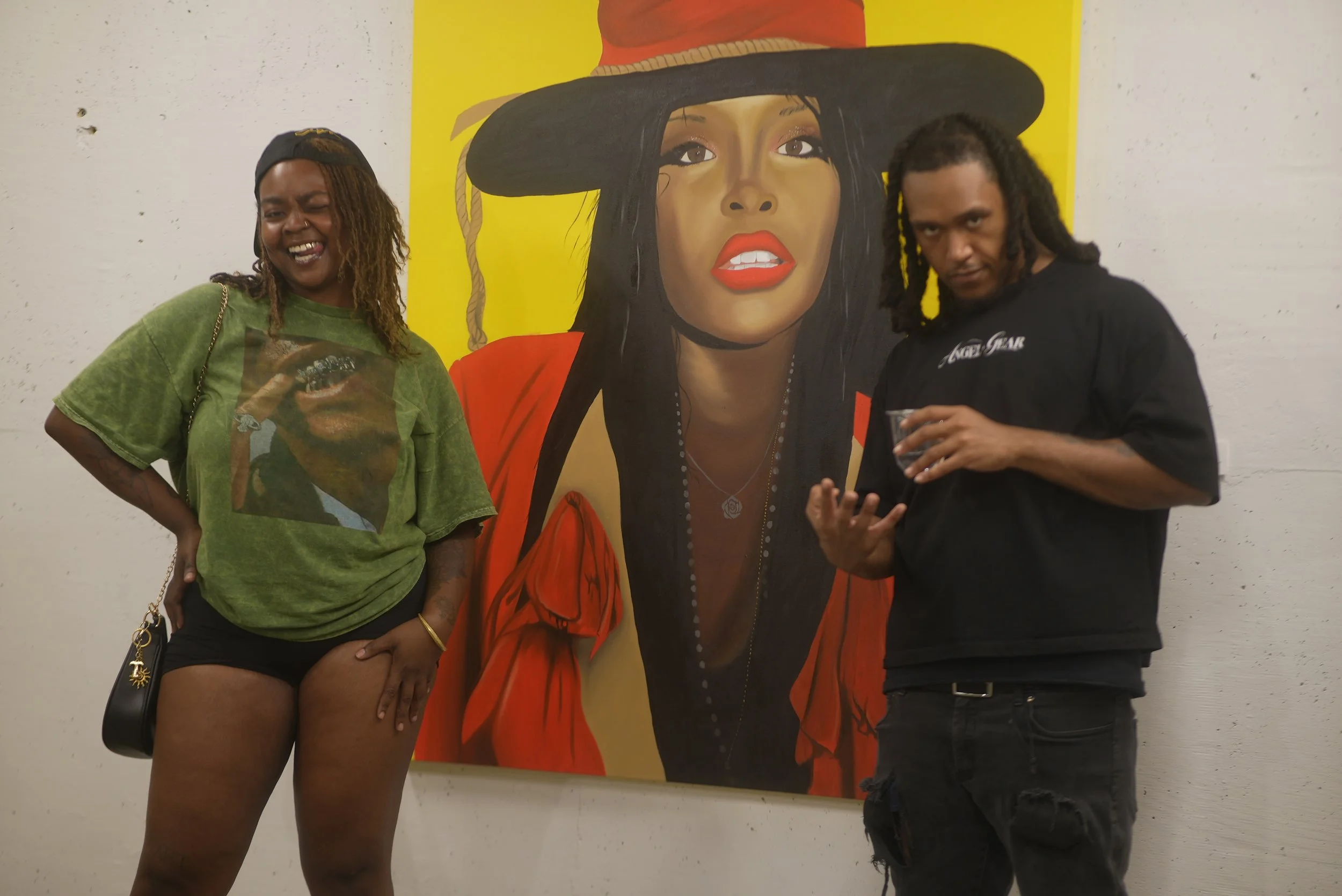 Two people standing in front of a large, colorful painting of a woman with dark hair, red lipstick, and wearing a large black hat, in an art gallery setting.