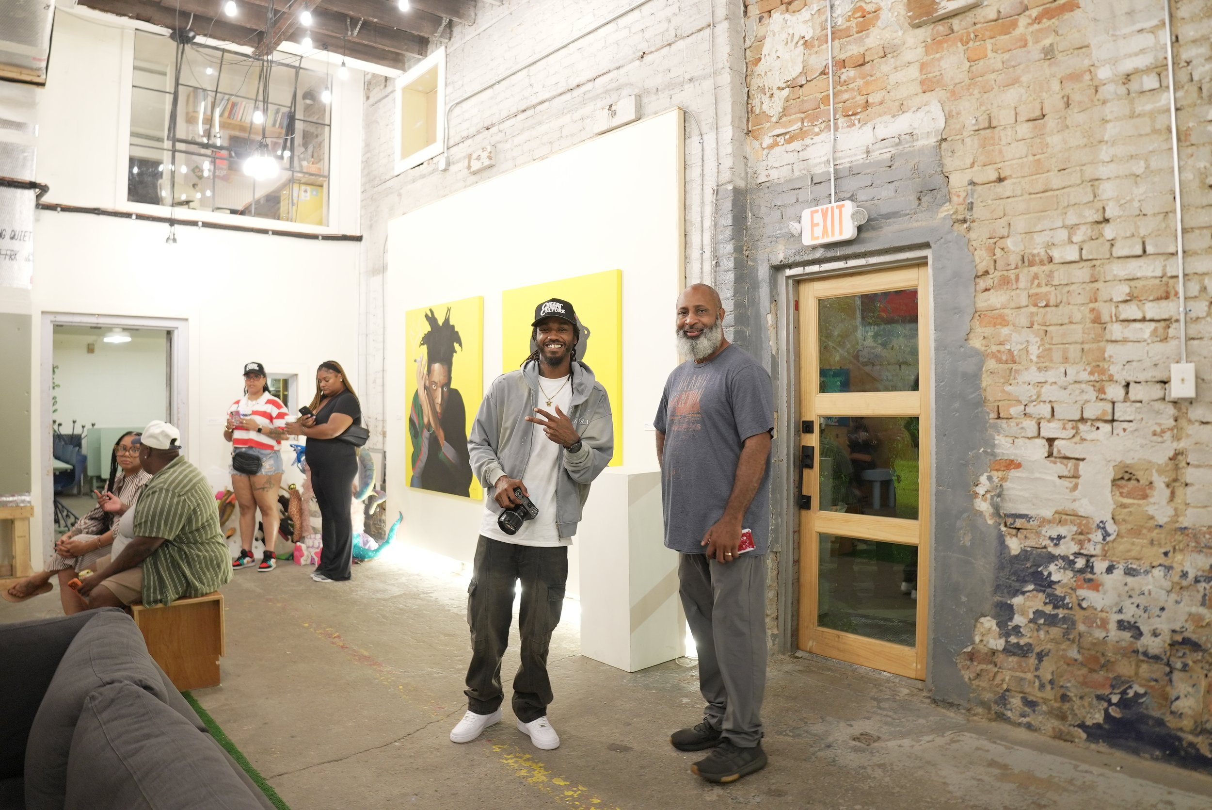 People gathered in an indoor industrial-style space with exposed brick walls, some standing and some sitting, during a social event or gathering.