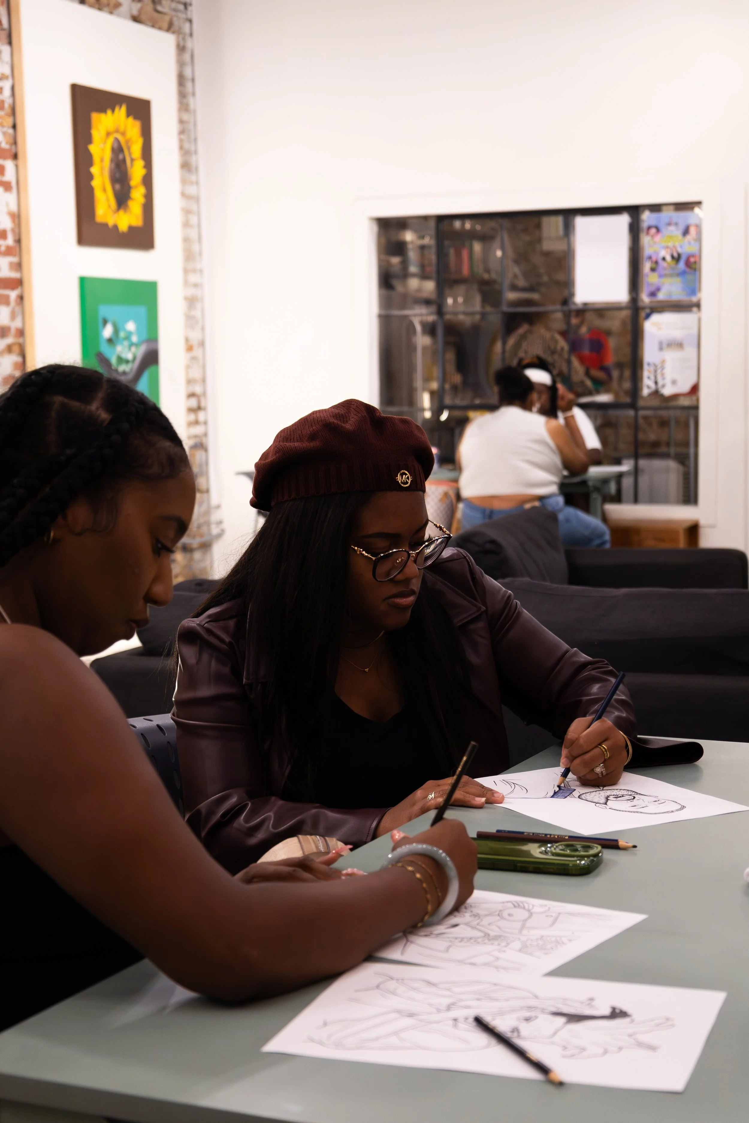 People sitting at a table drawing fashion sketches in an art studio.