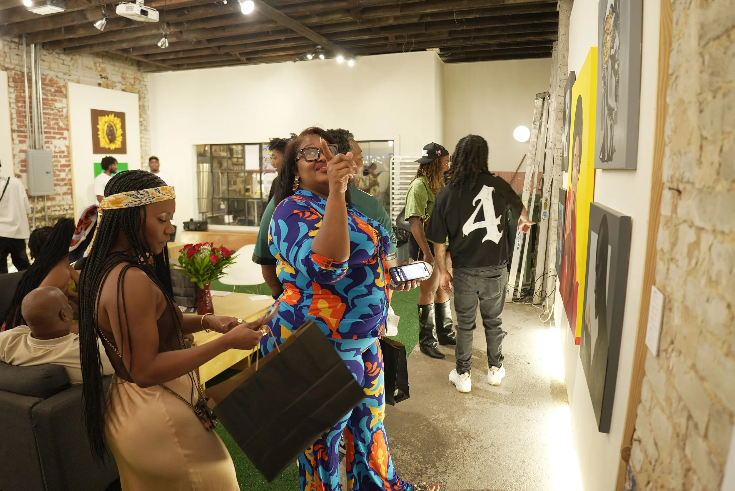 People viewing artwork at an art gallery or exhibition, with some individuals engaged and others examining the art.