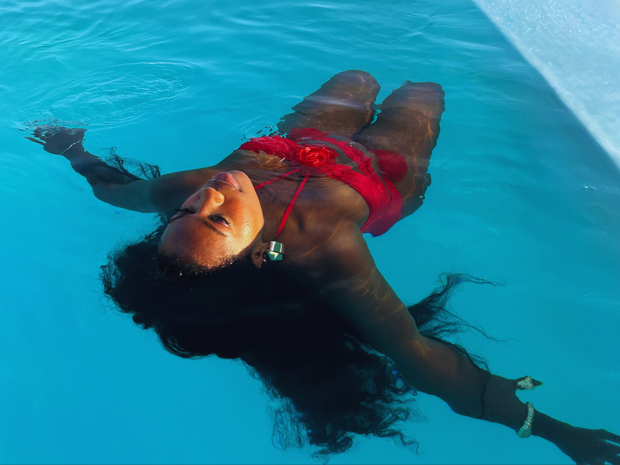 A woman laying on her back floats peacefully in a swimming pool, wearing a red swimsuit with her eyes closed.