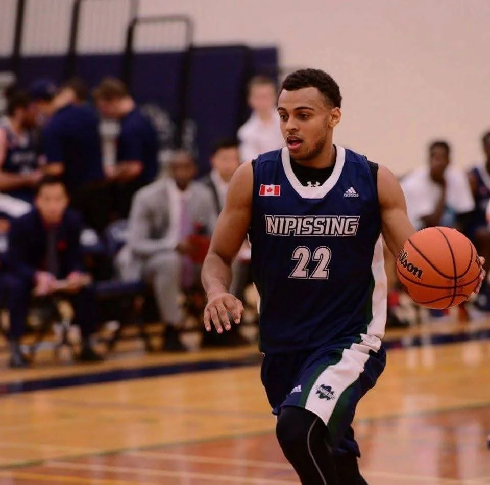 A young man wearing a navy blue basketball uniform with the number 22 is dribbling a basketball on the court during a game.
