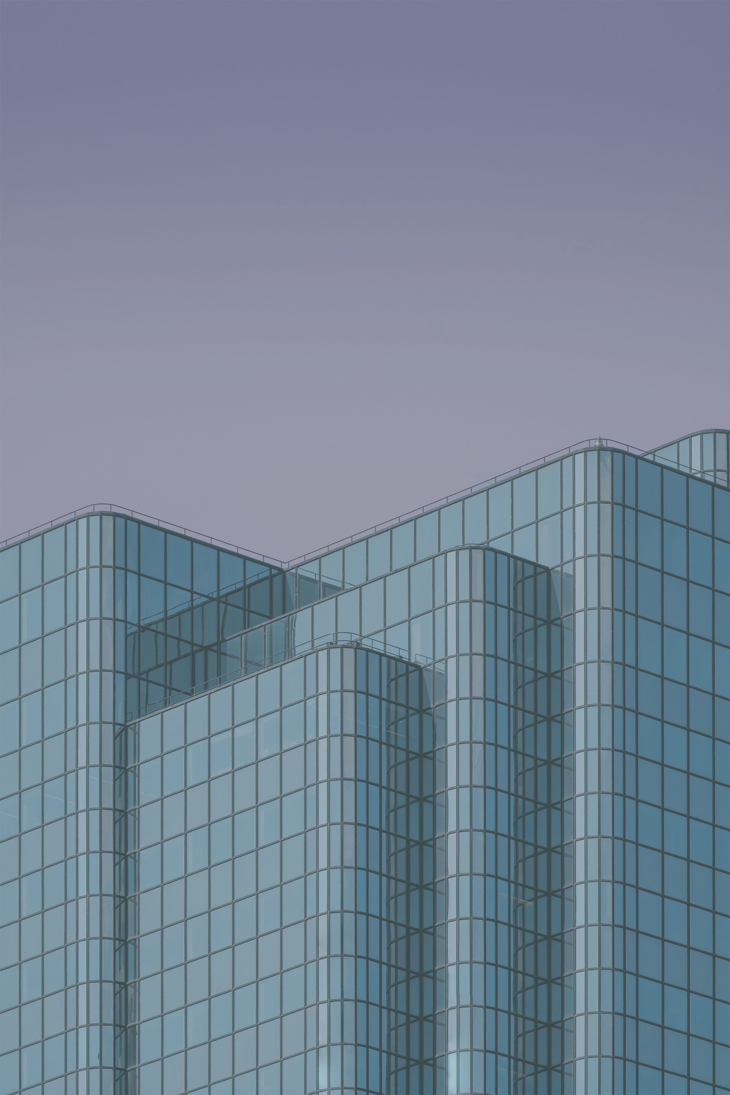 Close-up of a modern skyscraper with glass windows and curved architectural design against a clear, blue sky.