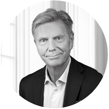 Black and white professional headshot of a man in a suit, with a calm facial expression, standing in front of vertical blinds.