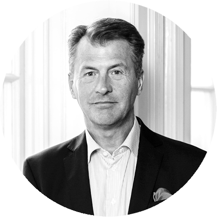Black and white portrait of a middle-aged man in a suit and collared shirt, standing in front of a draped curtain background.