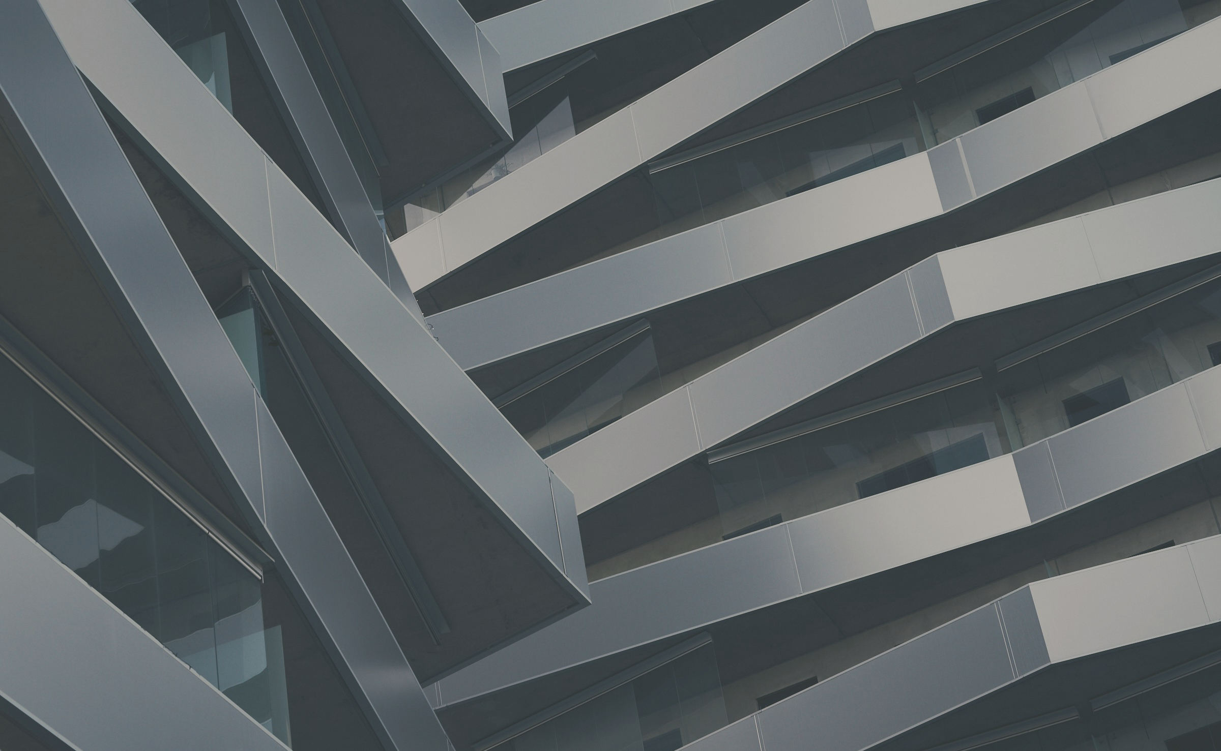 Close-up view of a modern multi-story building with angled glass windows and white panels, creating a geometric pattern.