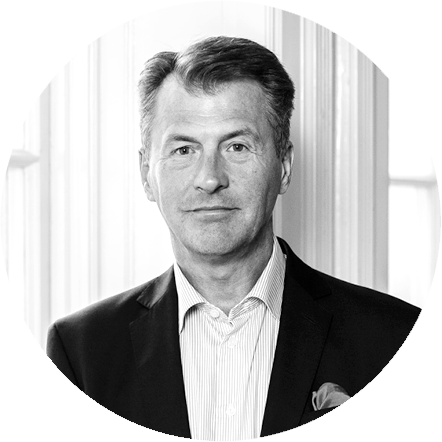 Black and white portrait of a middle-aged man in a suit and tie, standing in front of vertical blinds.