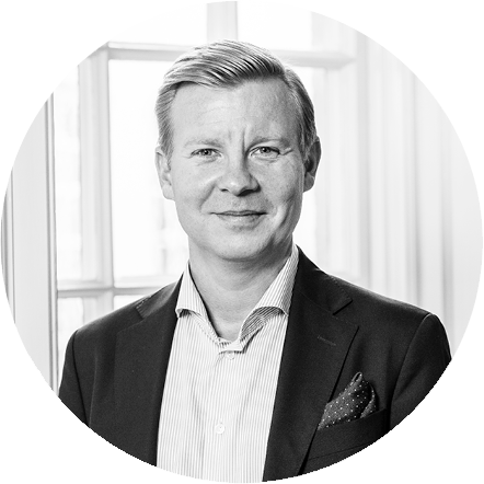 Black and white portrait of a man in a suit and tie, standing indoors near windows.
