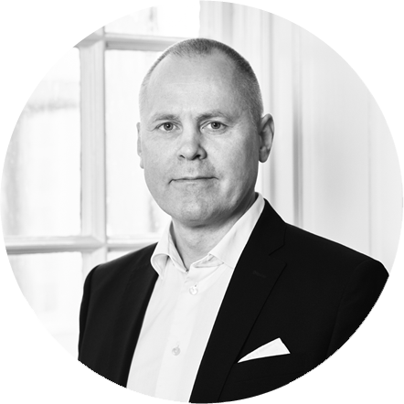 Black and white portrait of a man in a suit with a serious expression, standing in front of a window.