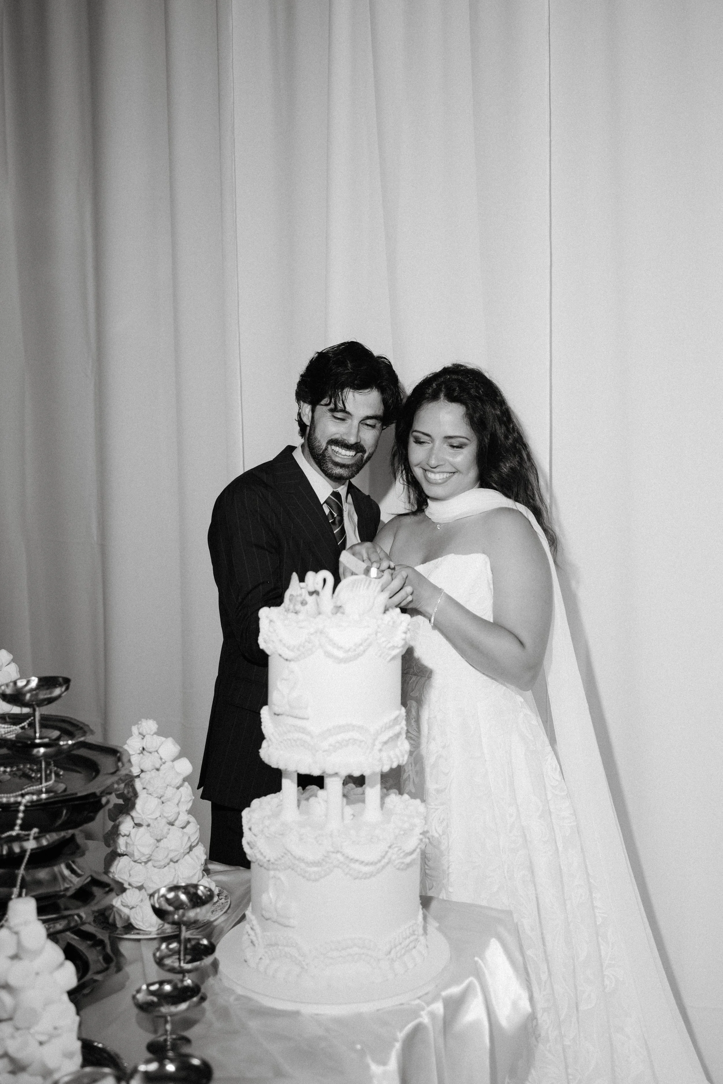Un couple marié souriant coupe un gâteau de mariage lors de leur réception.