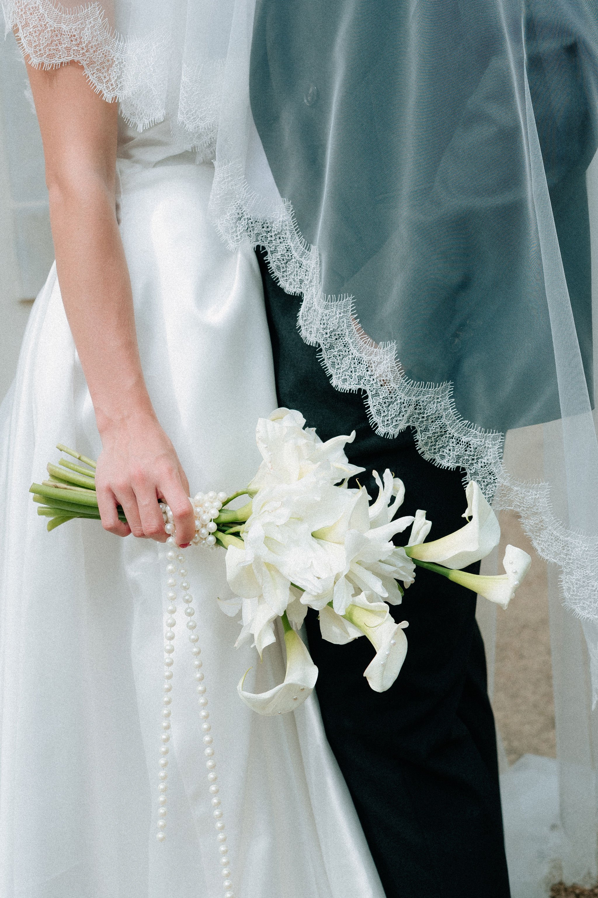 Personne portant une robe de mariée blanche avec des détails en dentelle et une personne portant des vêtements noirs, tenant un bouquet de fleurs blanches, composé principalement d'hibiscus et de jasmin.