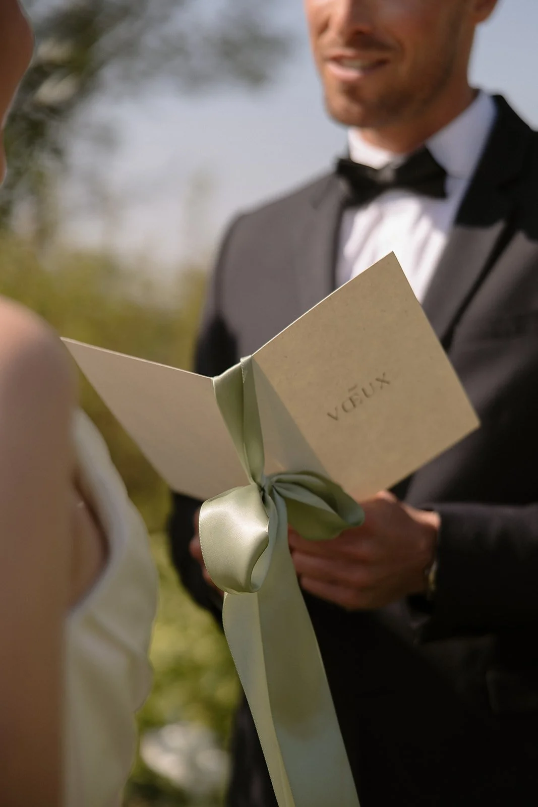 Un homme en smoking tend un livre à une femme lors d'une cérémonie de mariage en extérieur.