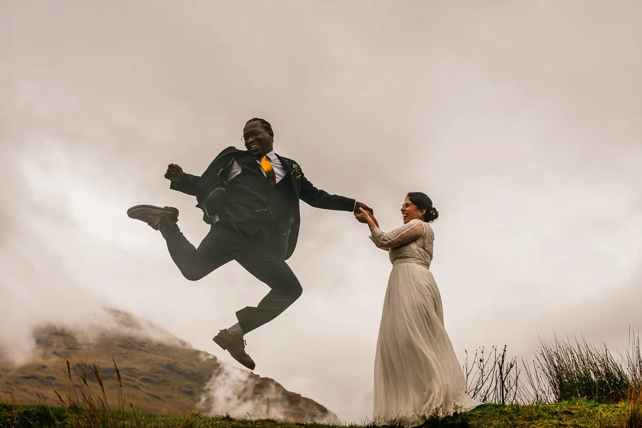 Fun-picture-of-a-bride-and-groom-jumping-in-the-air-on-top-of-a-Scottish-mountain