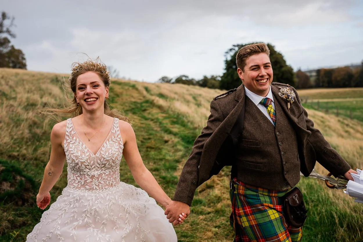 Bride-and-groom-laughing-running-down-hill-at-byre-at-inchyra