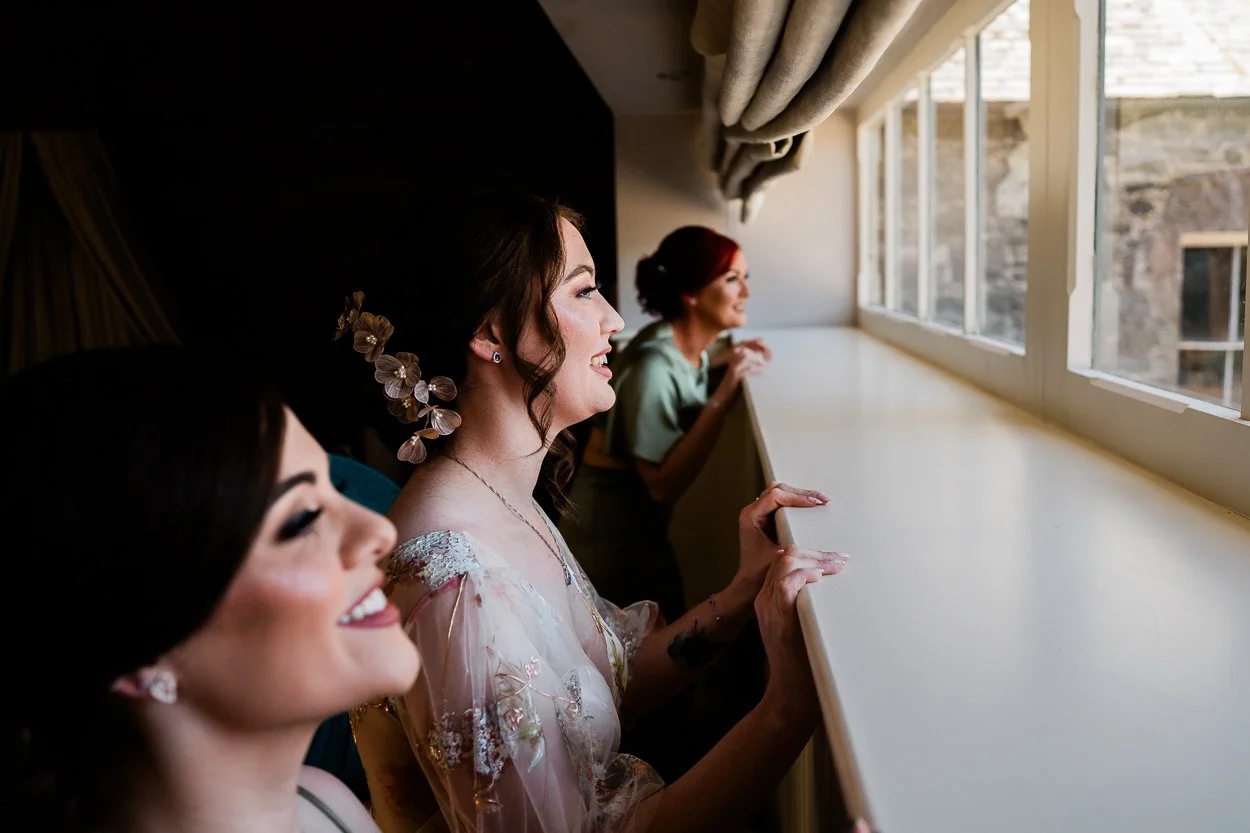 Bride-and-bridesmaids-watching-guests-arrive-through-window