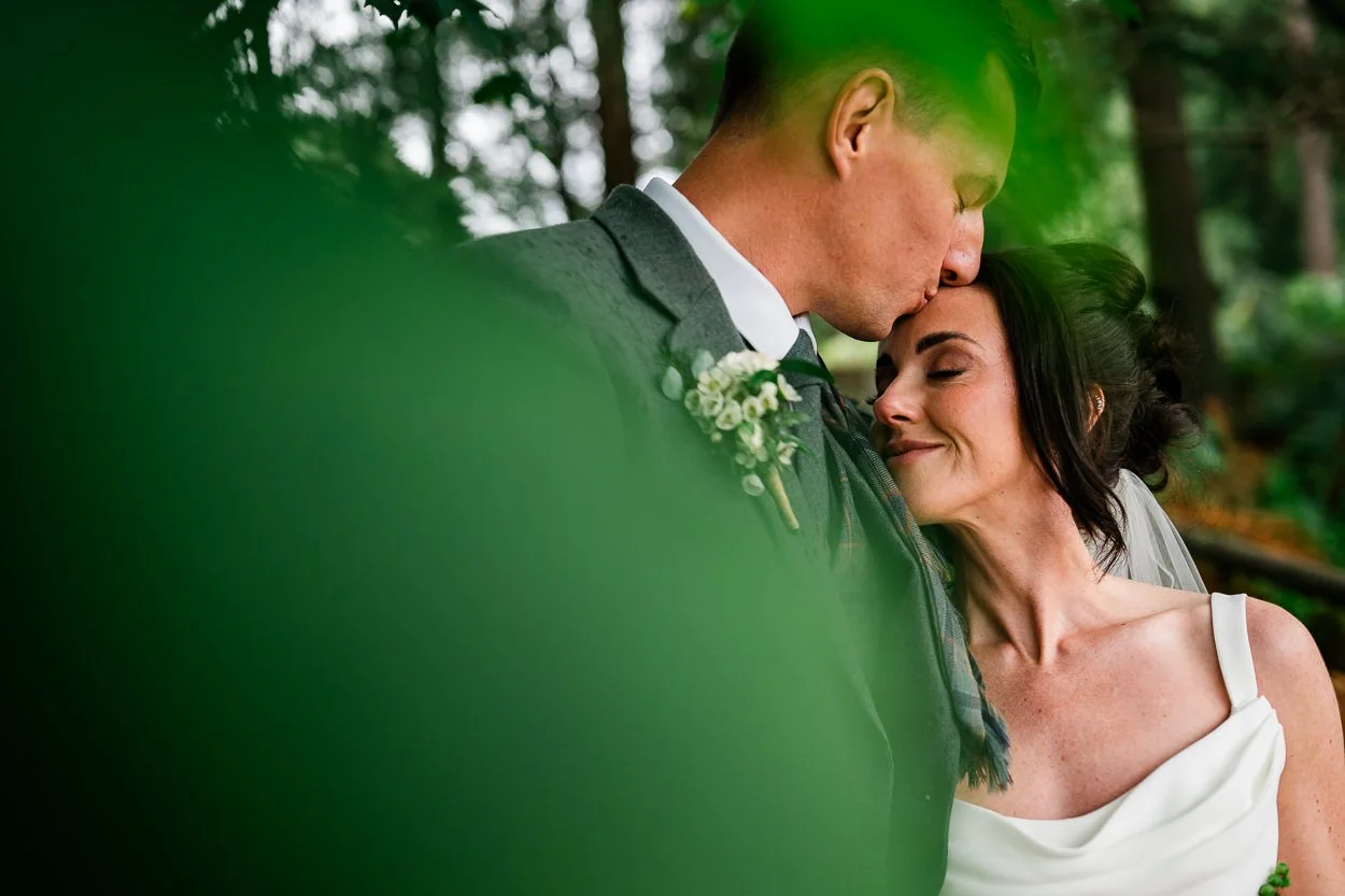 Romantic-moment-with-bride-and-groom-amongst-trees-cardney-steading