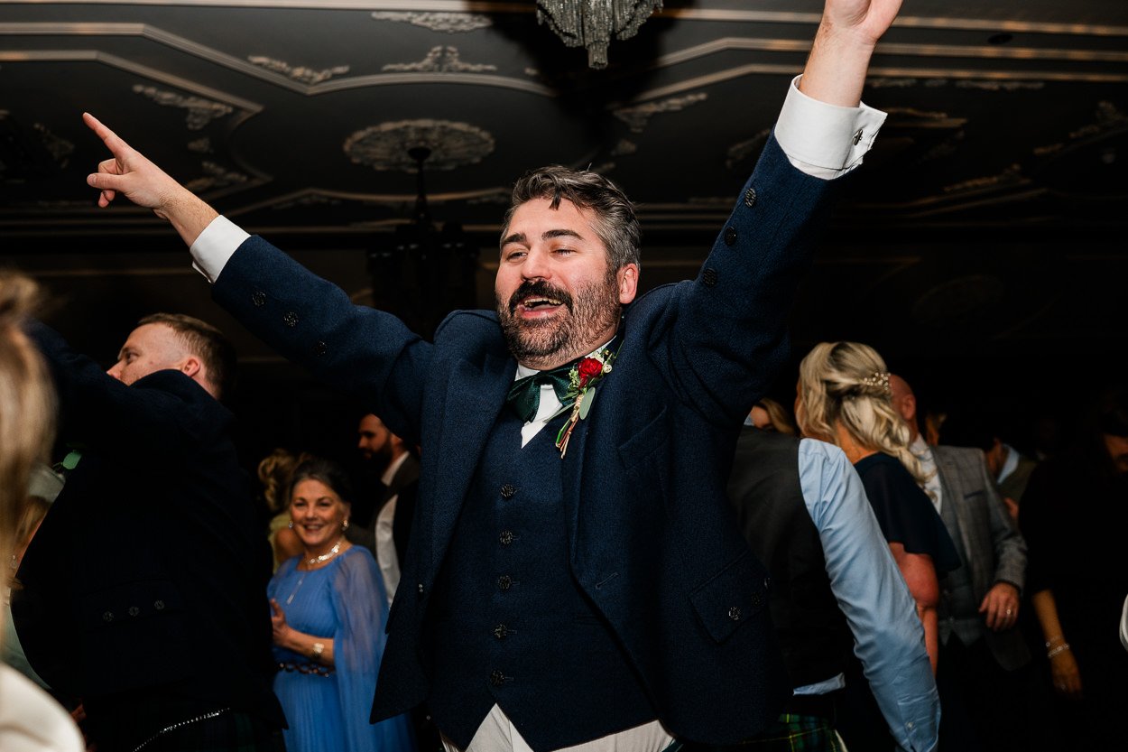 Groom with hands in the air on the dance floor