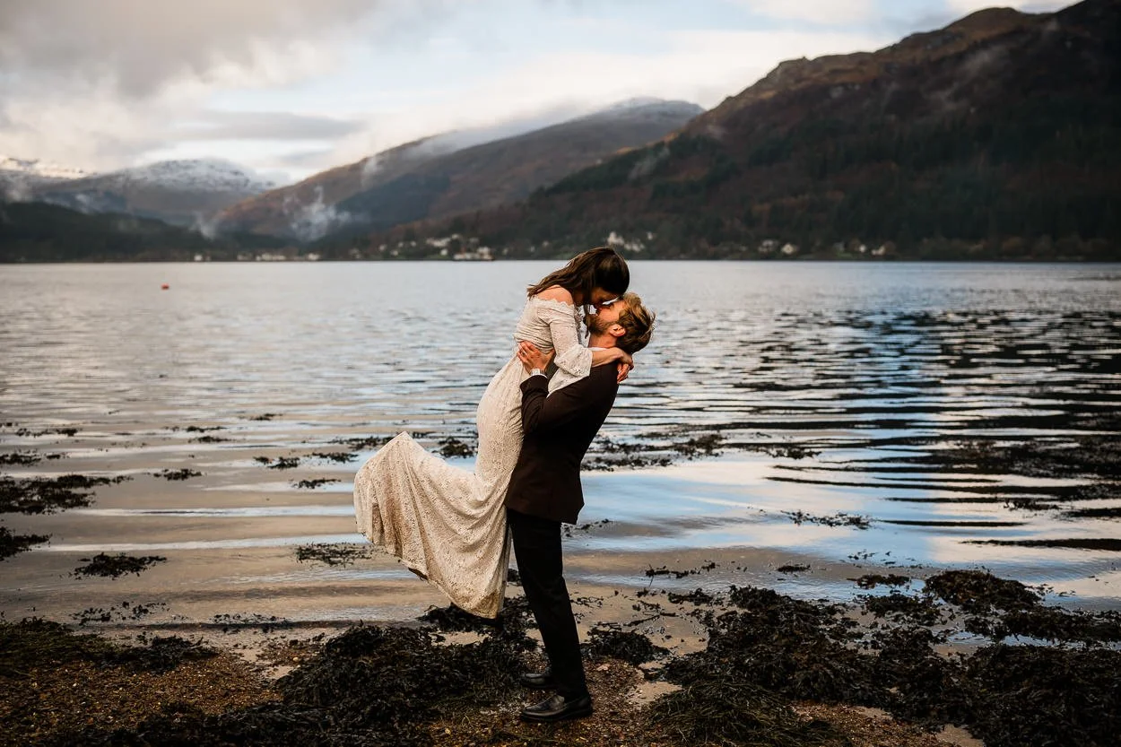 Groom-lifting-bride-in-the-air-for-kiss-with-loch-goil-backdrop