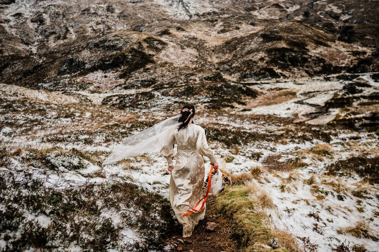 Bride in vintage dress walking away from camera through the snow
