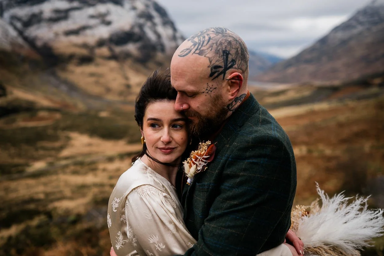 Groom-with-tattooed-head-embracing-bride-amongst-glencoe-wilderness