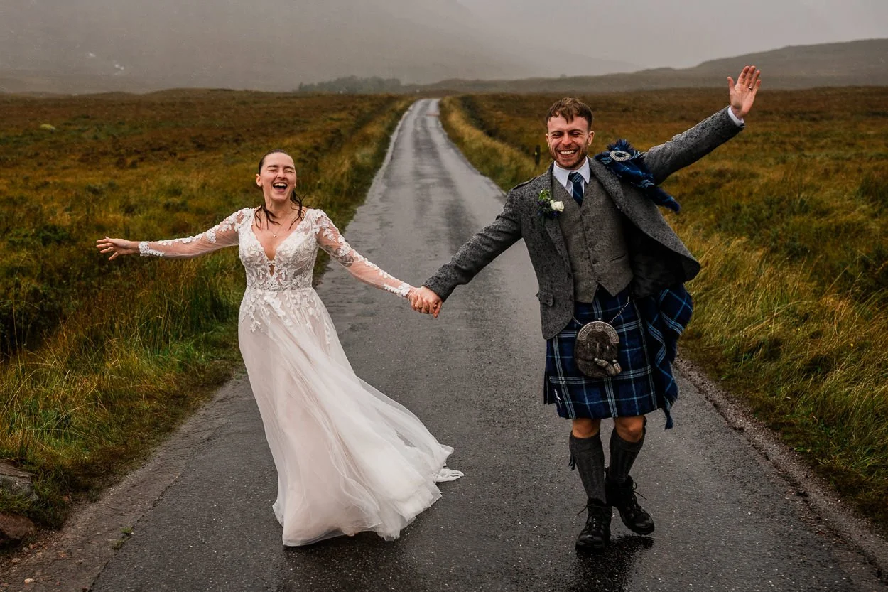 Fun picture of bride and groom walking down a road in Glencoe in the rain