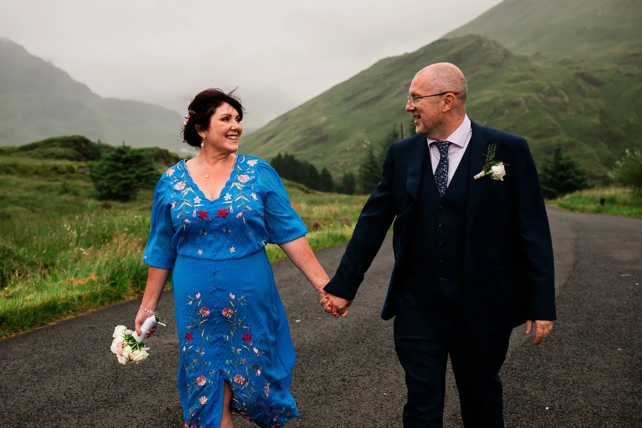Bride in blue dress walking down a road with groom laughing