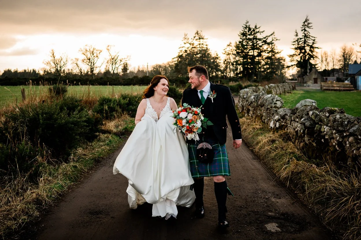 Bride-and-groom-walking-towards-camera-on-remote-Scottish-road