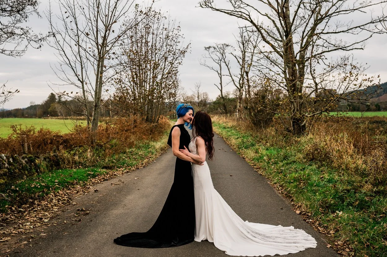 Two-brides-embracing-on-remote-Scottish-road