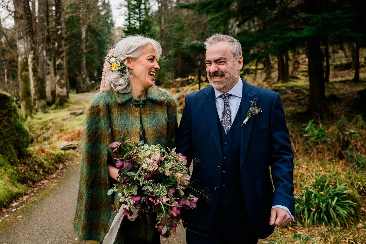 Bride in green dress walking with groom through trees laughing