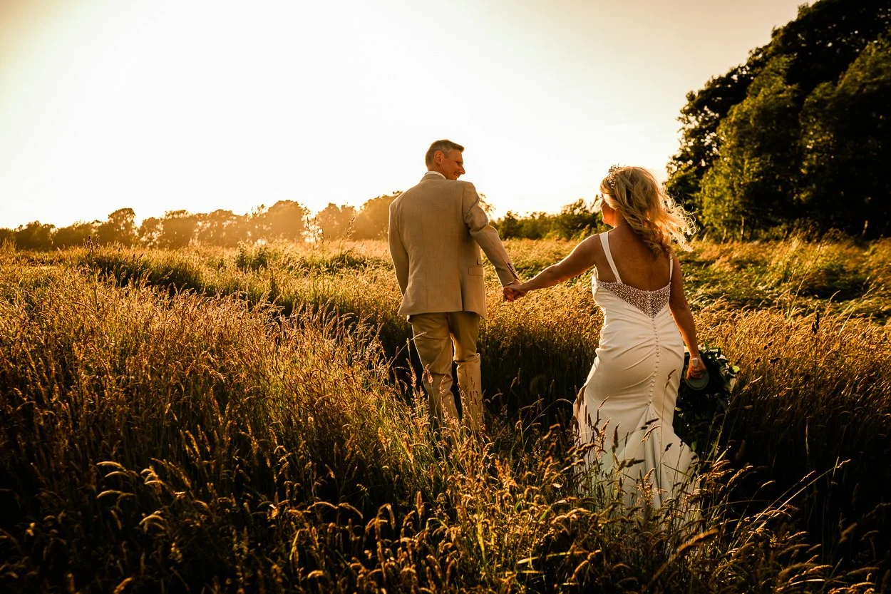 Bride-and-groom-walking-through-field-during-golden-hour-Rosebery-Steading