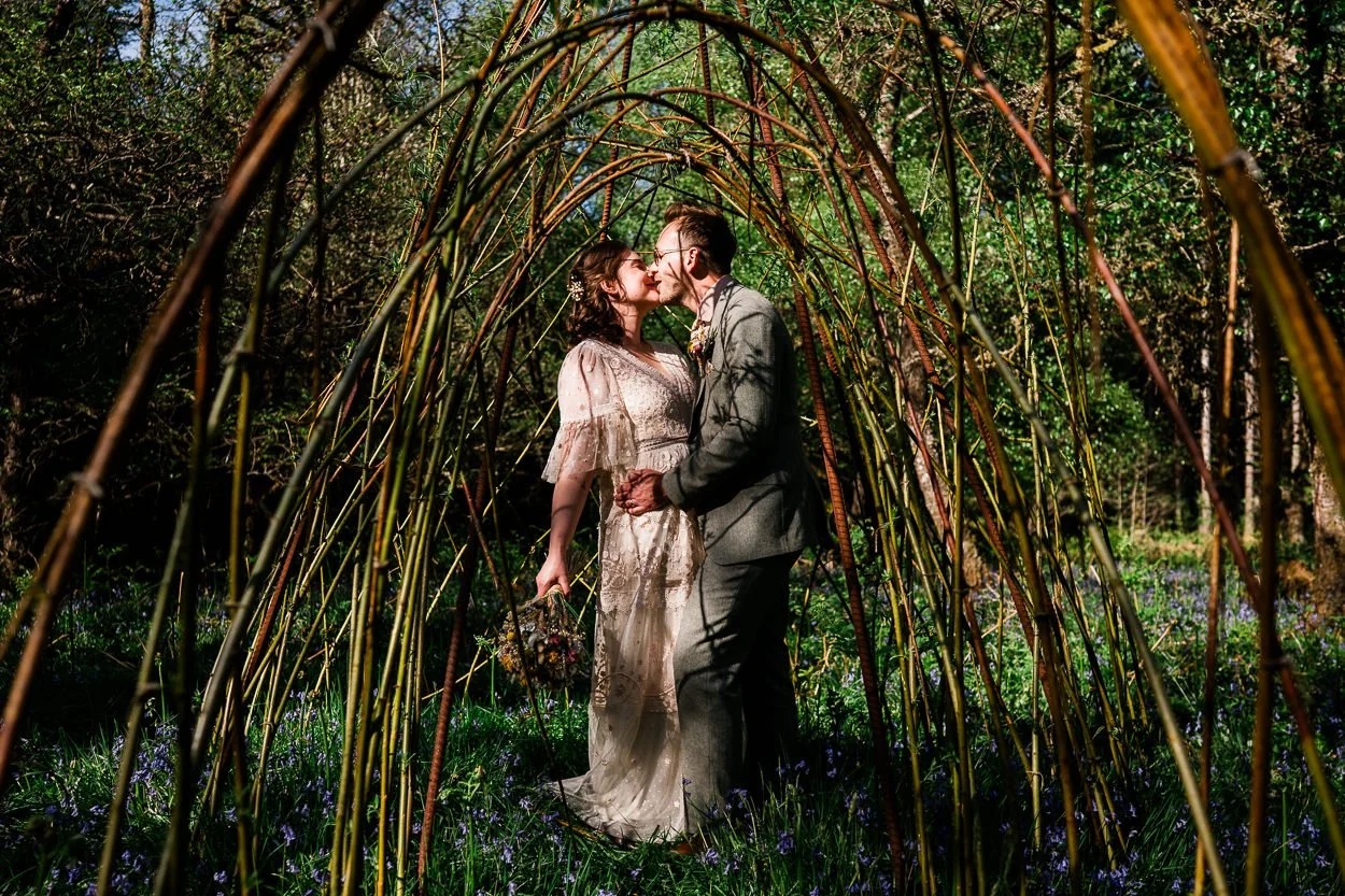Bride and groom kissing under tree arch in the woods