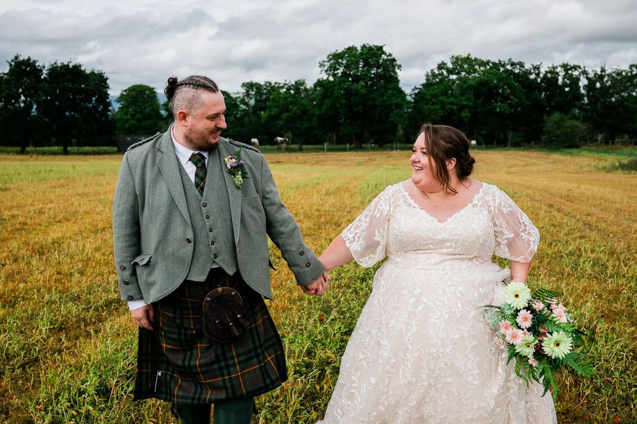Bride and groom walking through a field holding hands