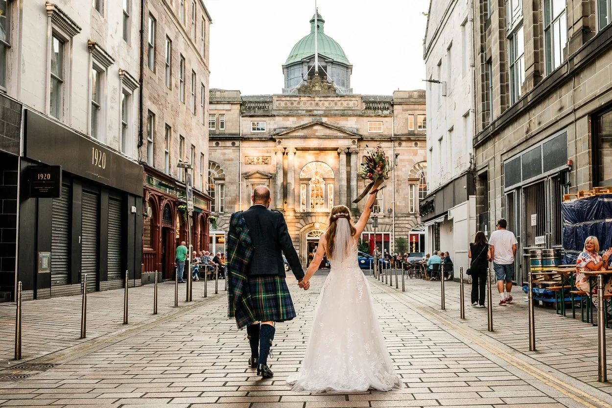Bride and groom walking towards Trades Hall Glasgow with the brides flowers in the air