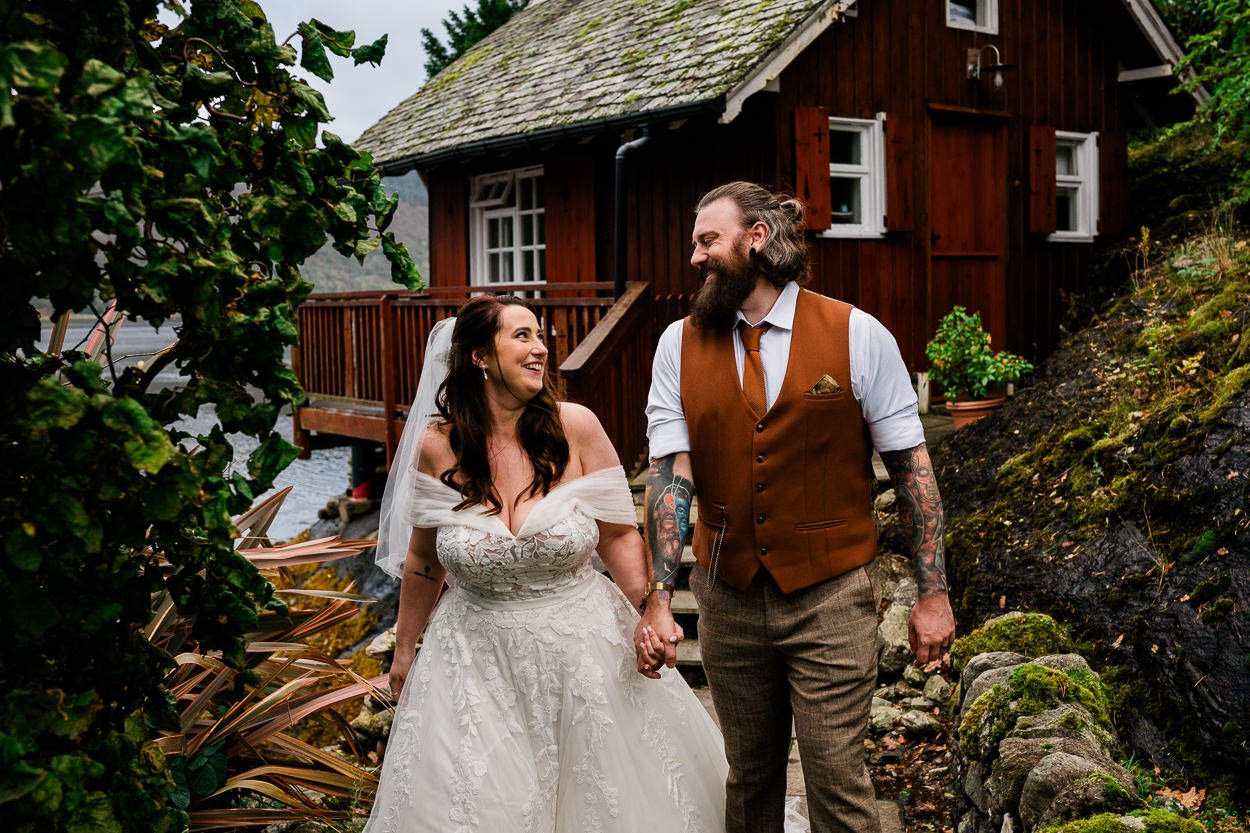 Bride and groom walking away from a loch side cabin laughing