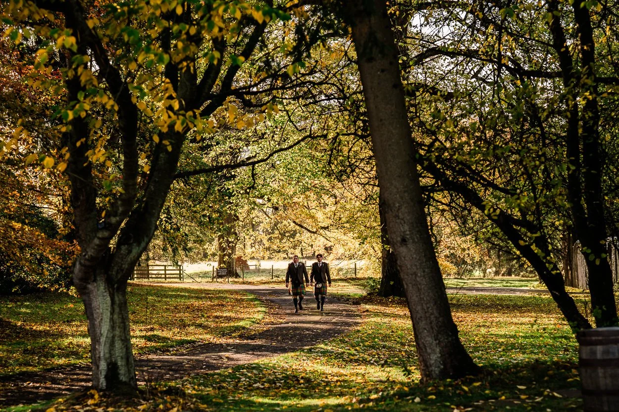 Groomsmen walking through trees in autumn light