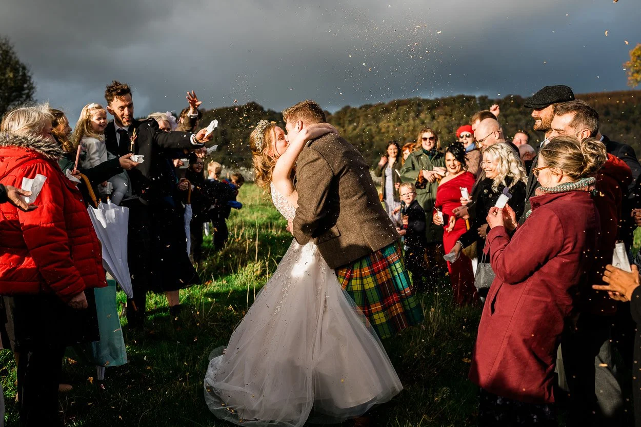 Bride and groom kissing during confetti toss at Byre at Inchyra