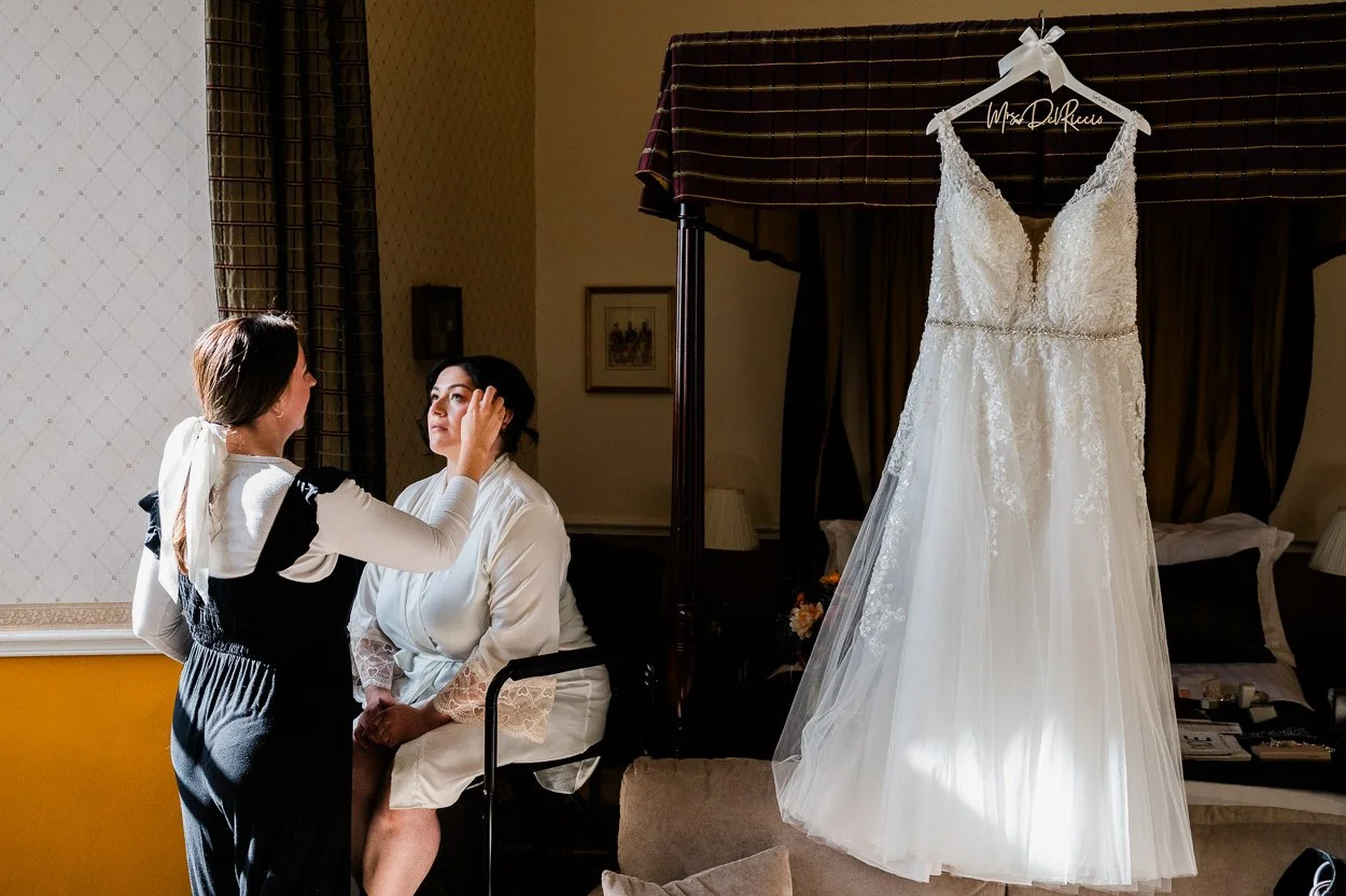 Bride getting makeup done with wedding dress in background