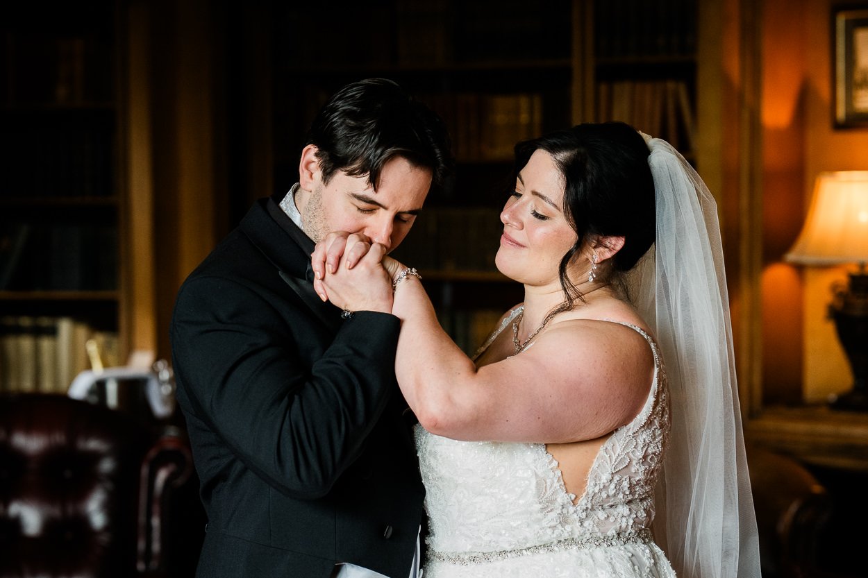 Groom kissing brides hand in library at Dalhousie Castle