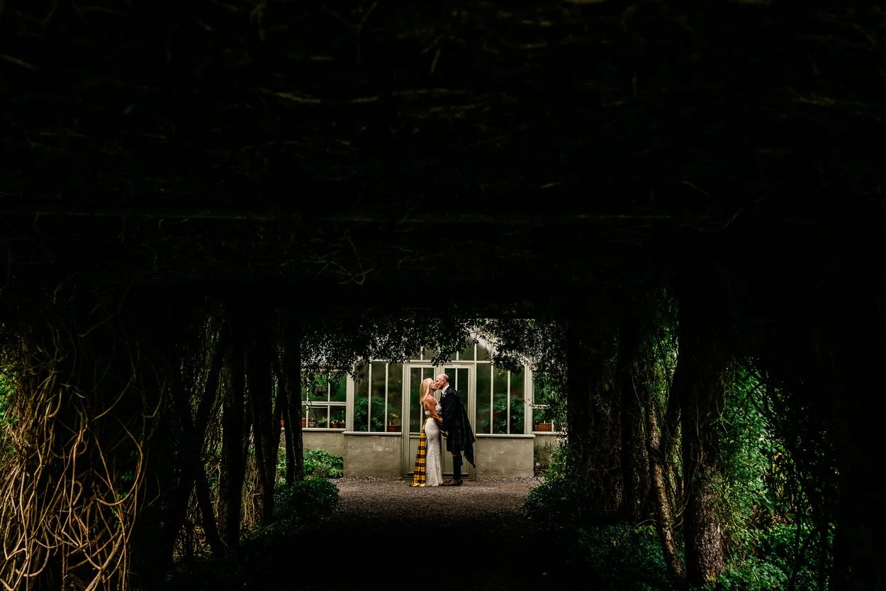 Creative portrait of bride and groom through trees at Dunvegan Castle