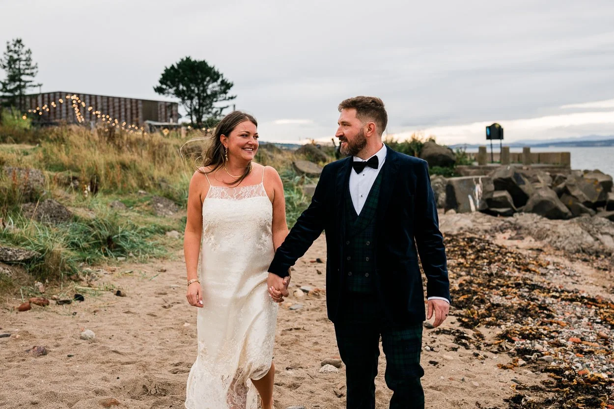 Bride and groom walk along beach in Leith