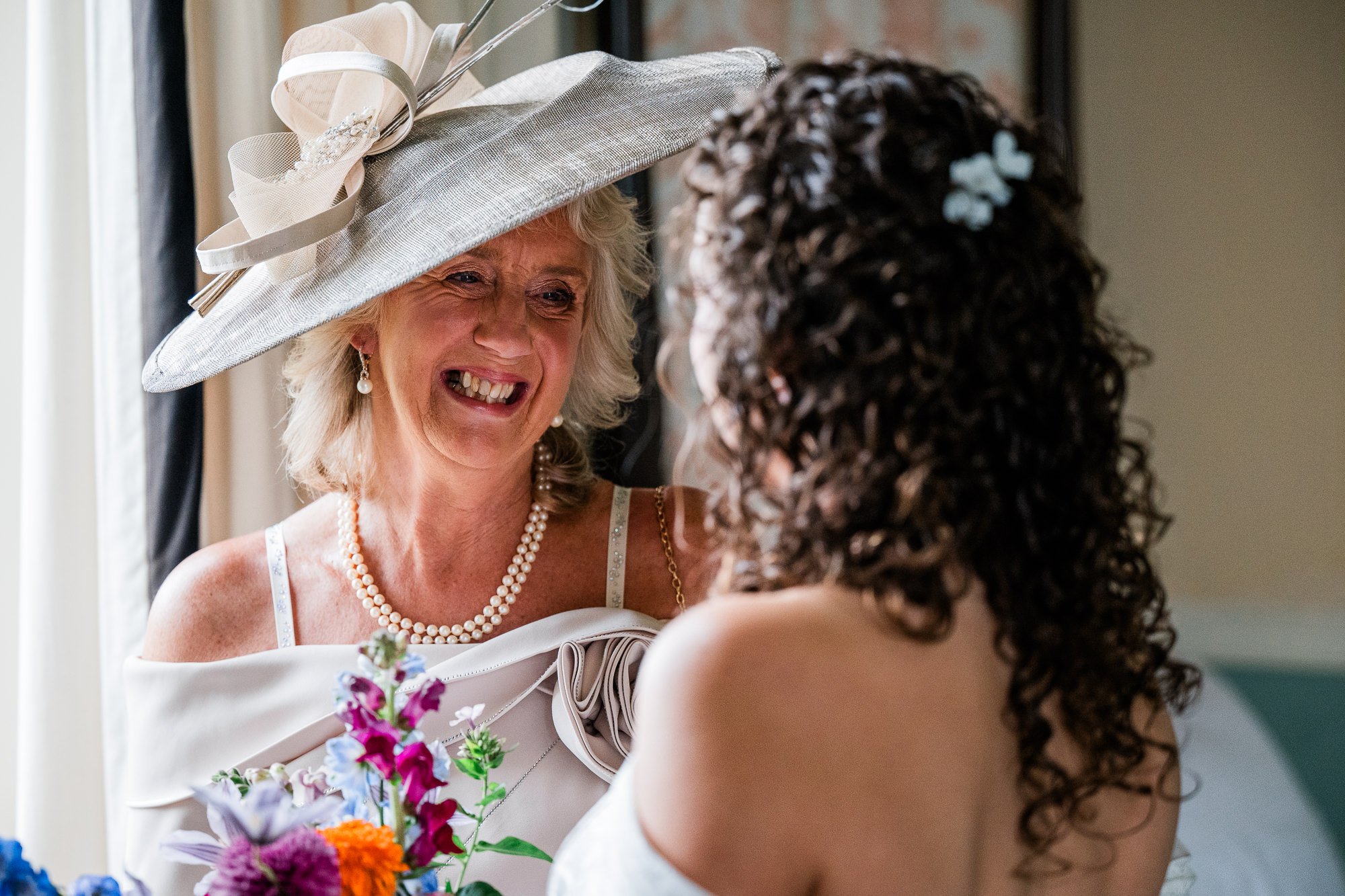 Aimee smiles with a wedding guest wearing a pale hat before the ceremony.