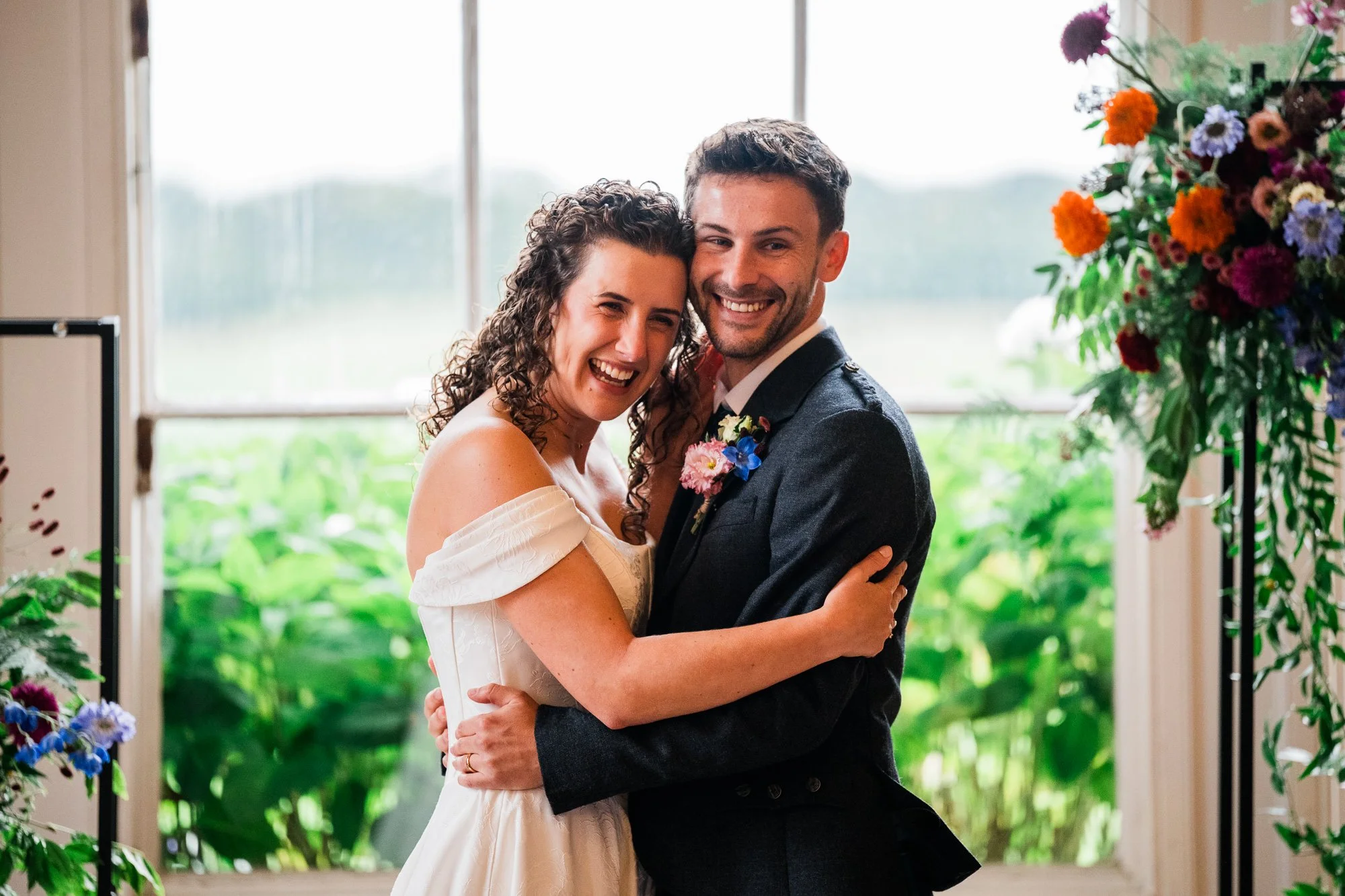 Aimee and Matthew embrace beside the floral arrangement after their ceremony.