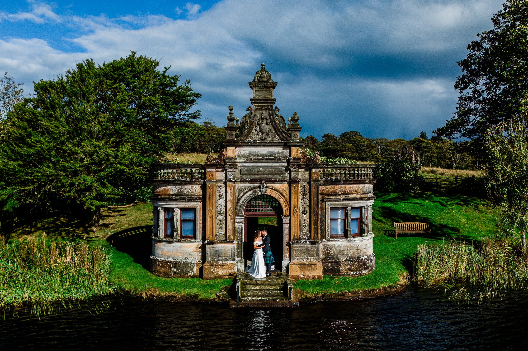 Aimee and Matthew stand at the entrance to the Bathing House beside the water.