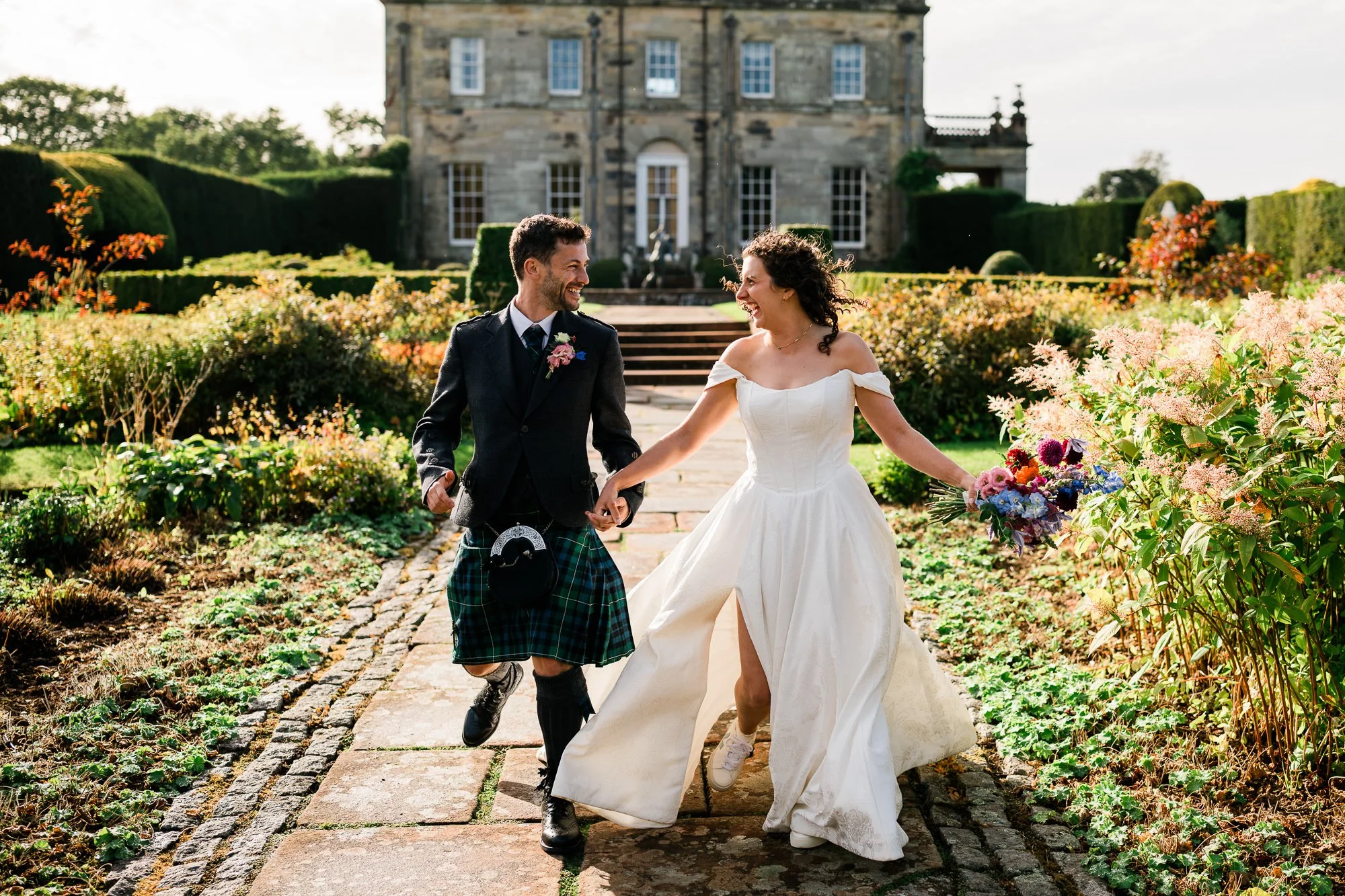 Aimee and Matthew walk hand in hand through the gardens in front of Kinmount House.