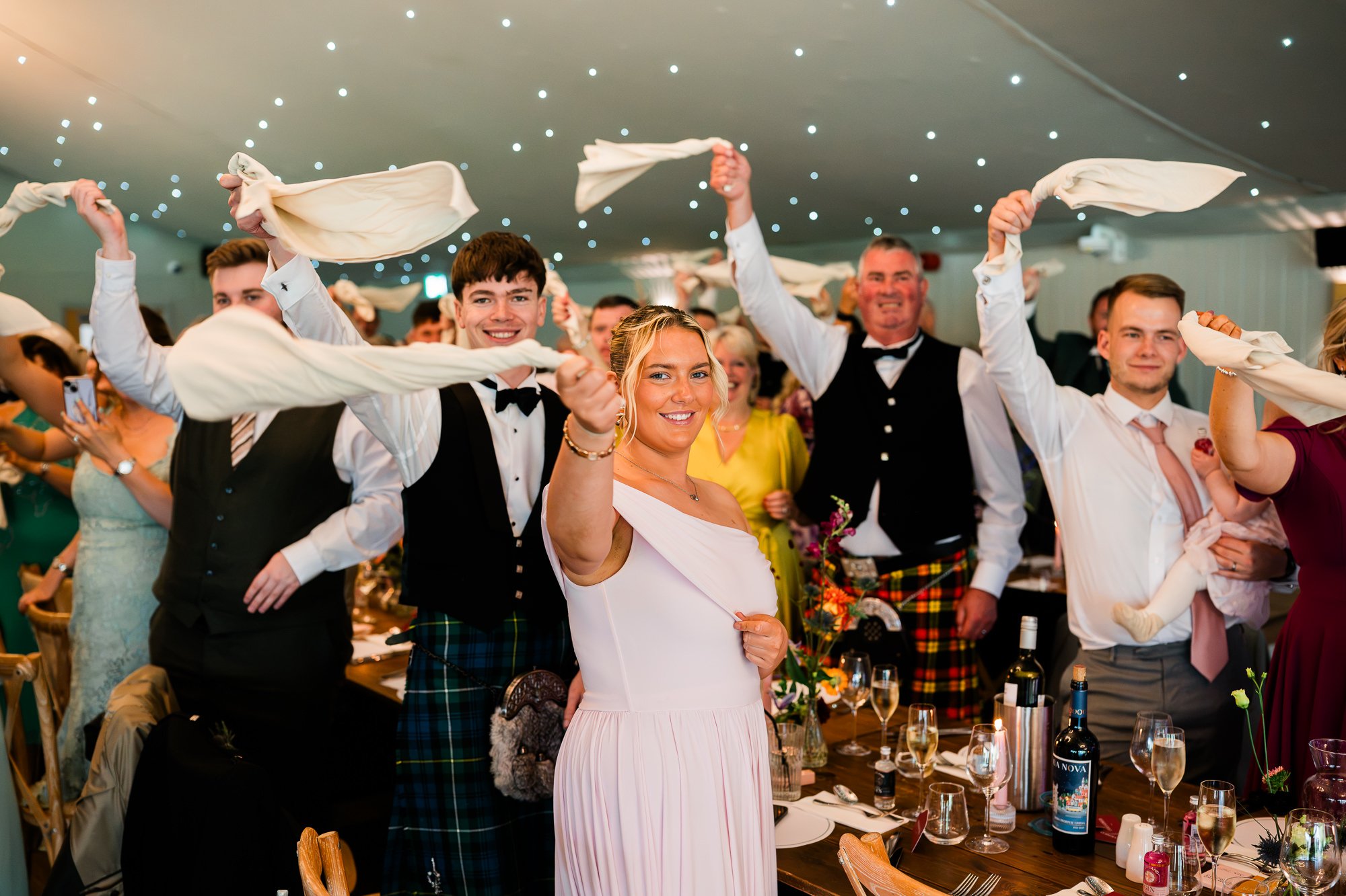 Aimee and Matthew raise their arms as guests welcome them to the wedding reception.