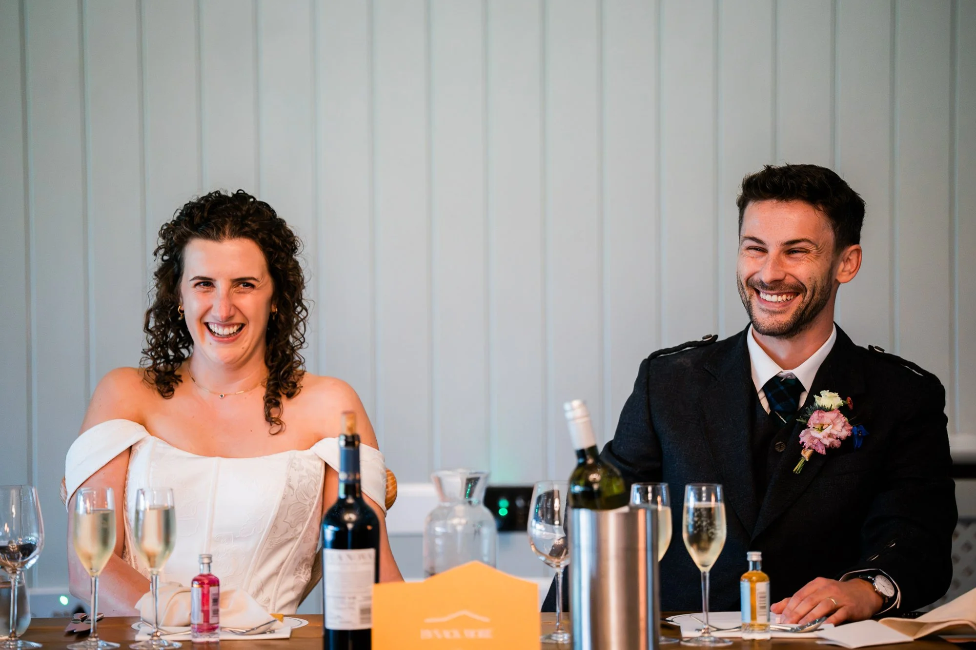 Aimee and Matthew smile together at the top table during their wedding reception.
